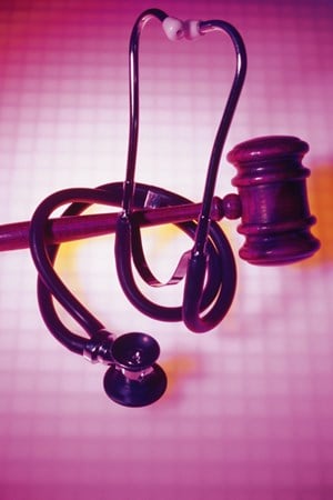 A wooden gavel with a stethoscope wrapped around it and an abstract pink and white grid background