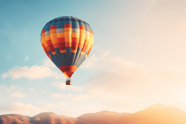 Colorful Hot Air Balloon Floats Above Mountaintops Against a Muted Partly Cloudy Sky 