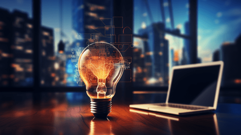 Laptop computer and glowing lightbulb on desk in front of window showing cityscape