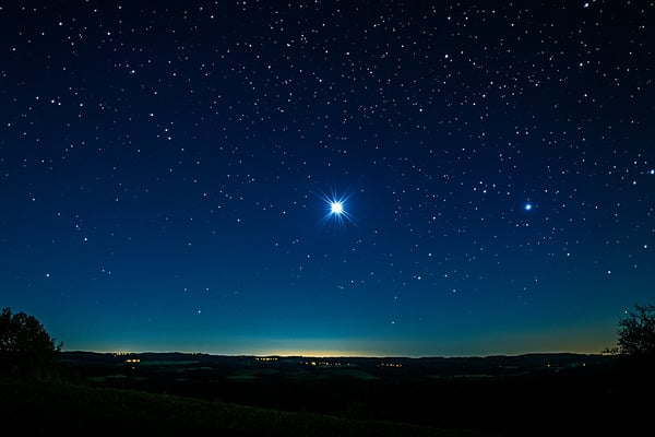 A single bright star shining in a clear night sky above the horizon.