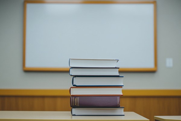 A stack of six textbooks with a blank whiteboard in the background.