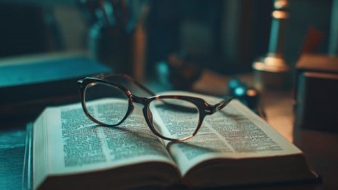 Open dictionary on desk with reading glasses sitting on top