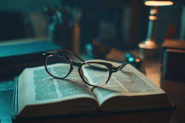 Open dictionary on desk with reading glasses sitting on top
