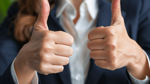 Closeup of the hands of a businesswoman wearing a dark blue suit giving two thumbs up