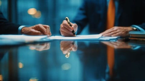 businesspeople's hands signing documents on a conference table with clear reflection underneath