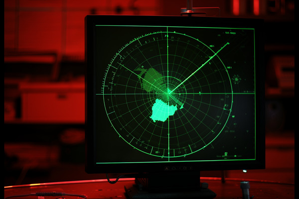 A green radar screen in a control room lit up with red light.