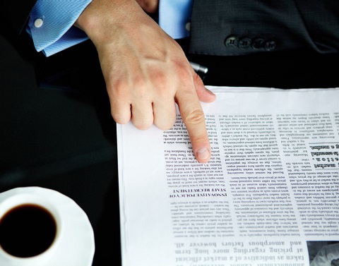 Hand pointing to line in newspaper with coffee