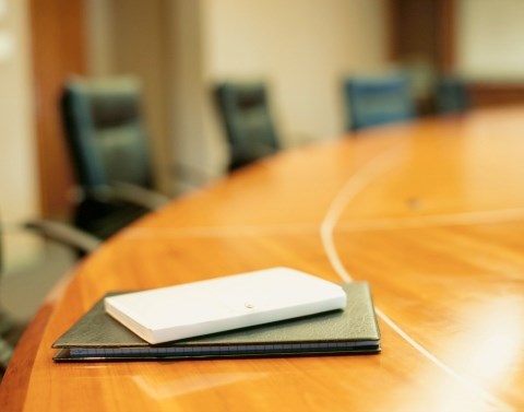 A round wooden conference table with black executive chairs around it and small black and white notebooks in one spot