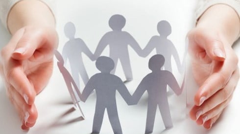 A set of protective hands around paper chain people in a circle