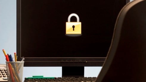 An office with a black computer monitor screen with a bright yellow lock, pencils, keyboard, phone, and chair