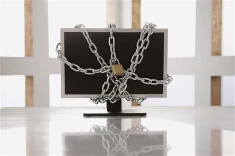 An office with a computer monitor on white desk with chains around it and locks attached to the chains on the front and back 