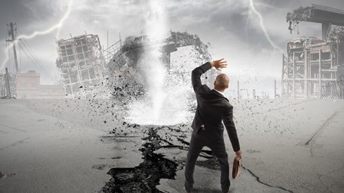 A businessman standing in front of a tornado and lightning strikes, shielding his face