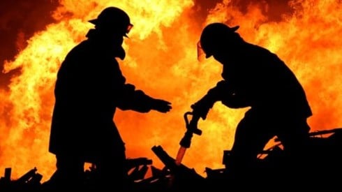 Two firefighters work to extinguish a raging fire