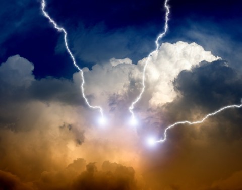 Blue sky with white and orange storm clouds emitting three white lightning bolts