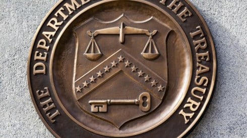 Metal sign mounted on a concrete block building showing THE DEPARTMENT OF THE TREASURY 1789 seal