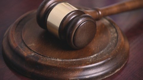A dark brown wooden gavel with a gold band around the middle resting on a worn wooden banging disc on a wood desk