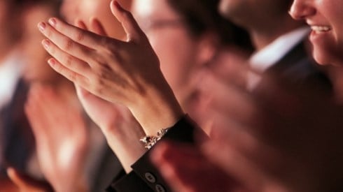 Group of people standing and applauding with one man clear and the rest of the people blurred