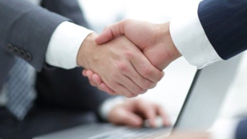 Two business people shake hands over a laptop