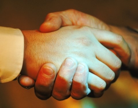 Men shaking hands with only the hands and a white dress shirt cuff visible and a blurred background