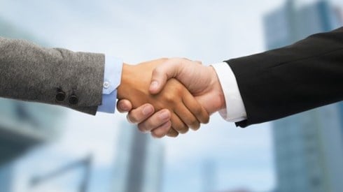 Two businessmen shaking hands with blurred skyscrapers in the background