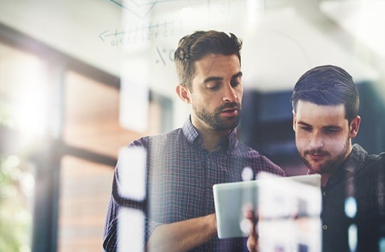 Two office colleagues discussing educational information viewing a tablet